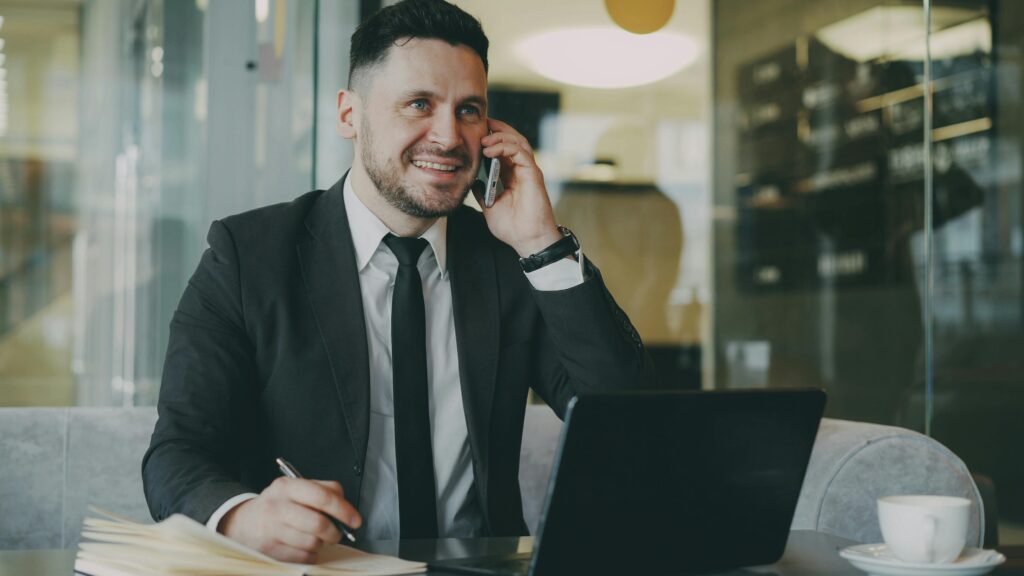Professional man in a suit talking on the phone and working on a laptop indoors.
