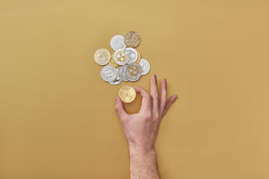 Hand holding coins with various cryptocurrencies on a yellow background. Perfect for finance-themed designs.